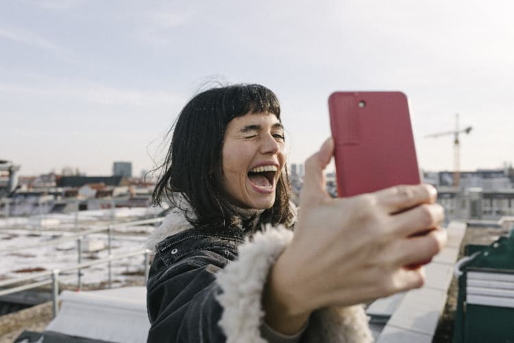Junge Frau auf einem Hausdach macht lachend ein Selfie von sich