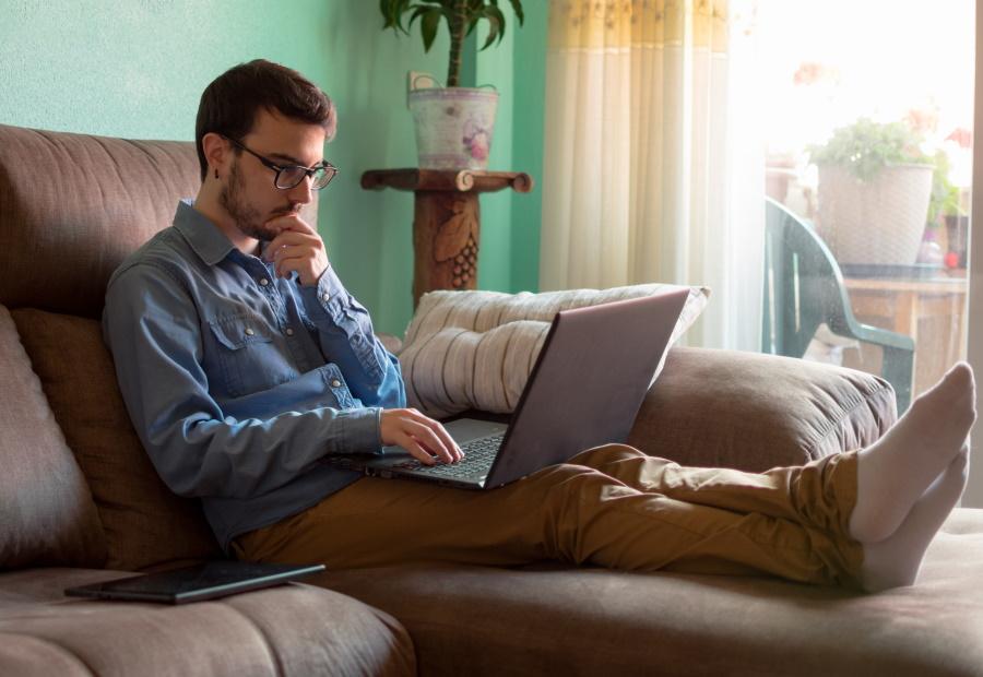 Mann sitzt auf der Couch mit Laptop und informiert sich 