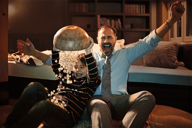 Vater und Sohn schauen begeistert Fernsehen und verschütten dabei Popcorn