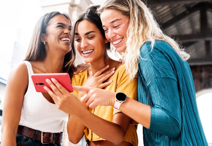 Drei junge Frauen schauen lachend auf ein Smartphone