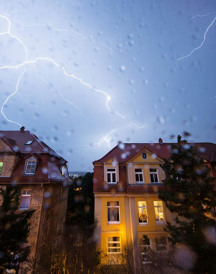 Über eine Wohnsiedlung zieht ein nächtliches Gewitter. Die Blitze erleuchten den Himmel. 