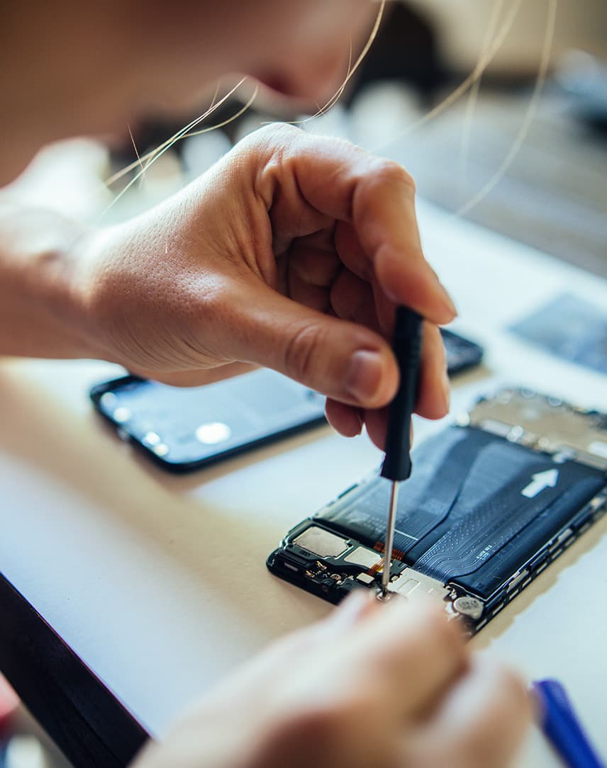 Eine Frau repariert ein Smartphone, das vor ihr auf dem Tisch liegt. 