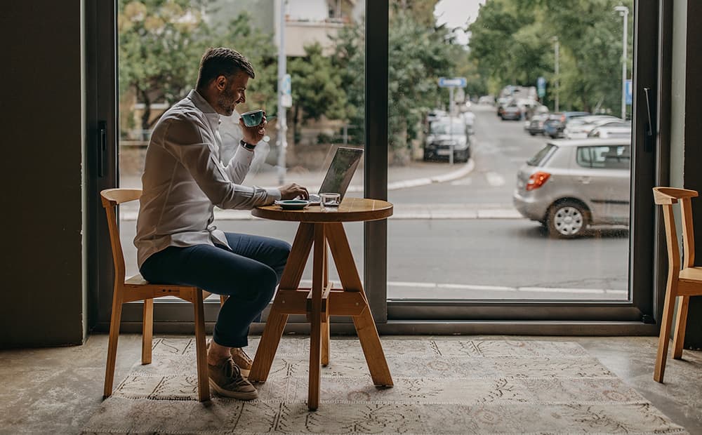 Ein Mann sitzt mit seinem Laptop in einem Cafe und arbeitet. 