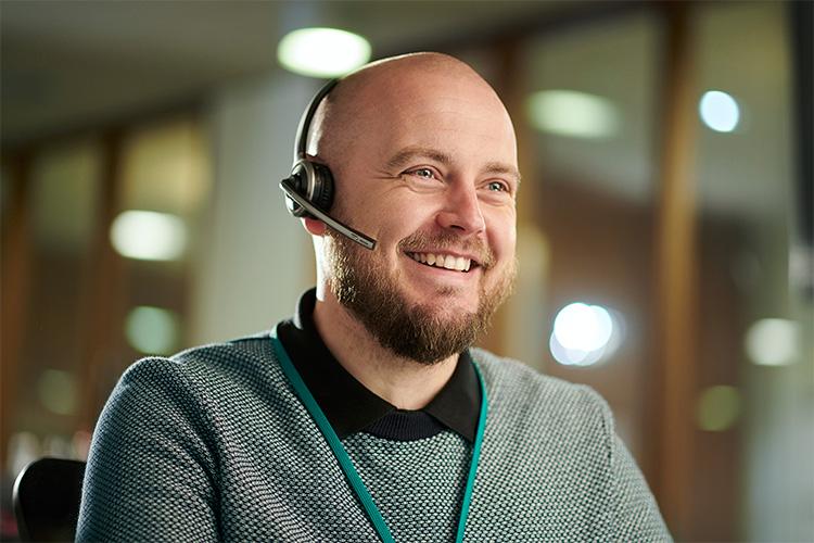 Ein Mann trägt ein Headset und lächelt, während er ein Telefonat führt.