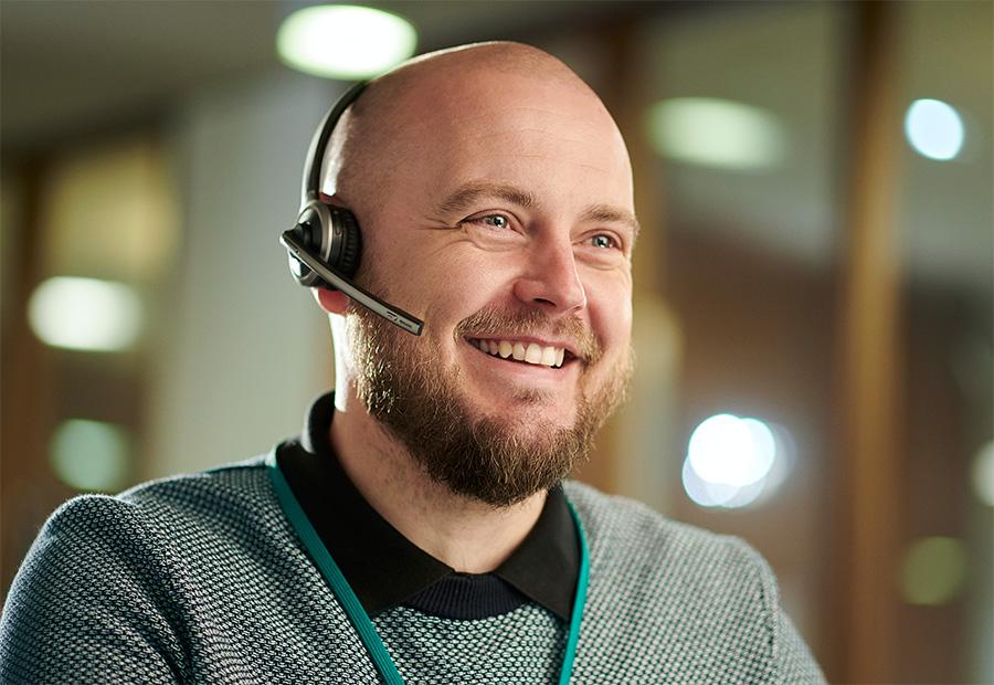 Ein Mann trägt ein Headset und lächelt, während er ein Telefonat führt.