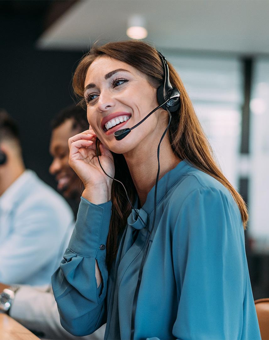 Eine Frau sitz mit anderen KollegInnen in einem Call Center. Sie telefoniert und lächelt, während sie auf den Bildschirm guckt.