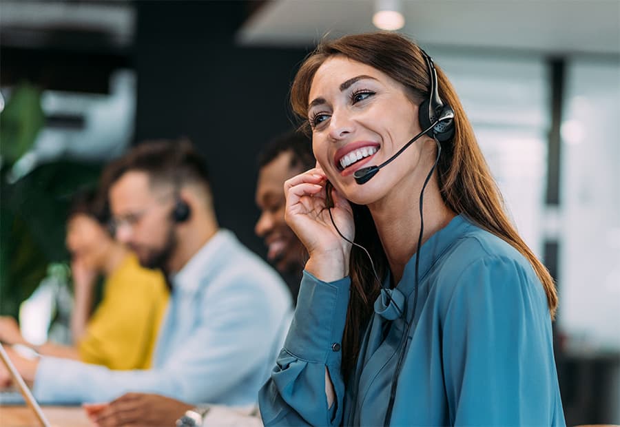 Eine Frau sitz mit anderen KollegInnen in einem Call Center. Sie telefoniert und lächelt, während sie auf den Bildschirm guckt.