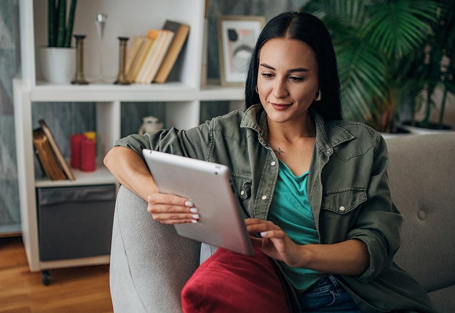 Eine Frau sitzt mit ihrem Tablet auf dem Sofa in ihrem Wohnzimmer.