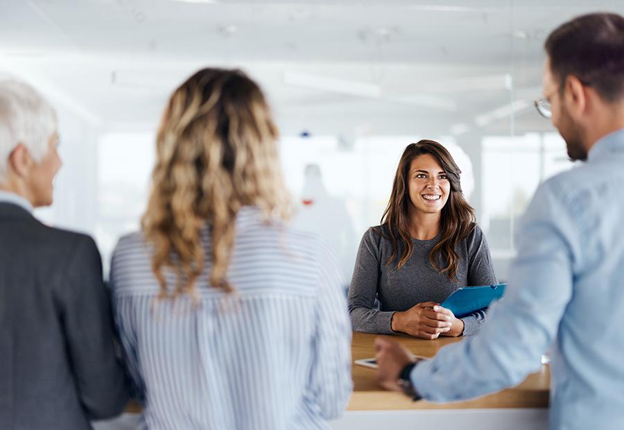Eine Frau sitzt in einem Besprechungsraum anderen Personen gegenüber und hält eine Mappe in der Hand.
