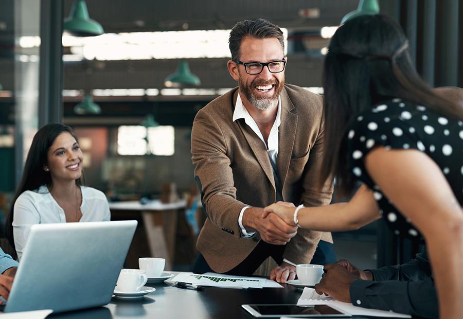Ein Mann schüttelt einer Frau die Hand. Sie sind in einem Besprechungsraum eines Büros.