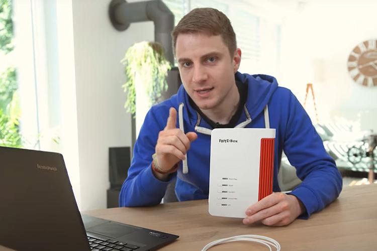 EWE-Smartgeber Jan sitzt im Wohnzimmer und hält einen Router in der Hand