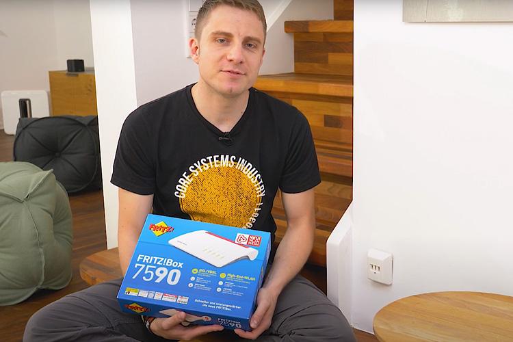 EWE-Smartgeber Jan sitzt im Wohnzimmer und hält einen Router-Karton in der Hand