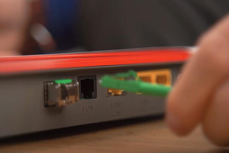 Eine Hand hält ein grünes Kabel, das mit einem Router verbunden wird