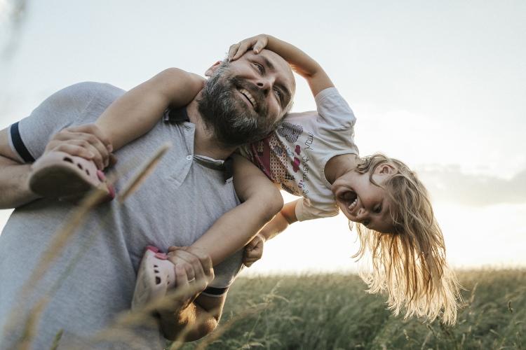 Kind lacht auf den Schultern des Vaters, im Hintergrund ist ein Windrad