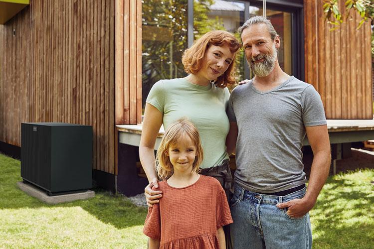 Familie steht vor Ihren Haus, neben dem sich eine Wärmepumpe befindet