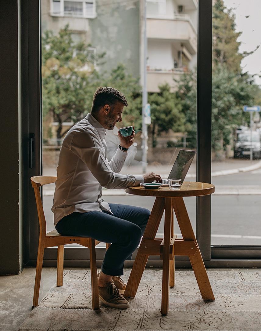 Ein Mann sitzt mit seinem Laptop in einem Cafe und arbeitet.